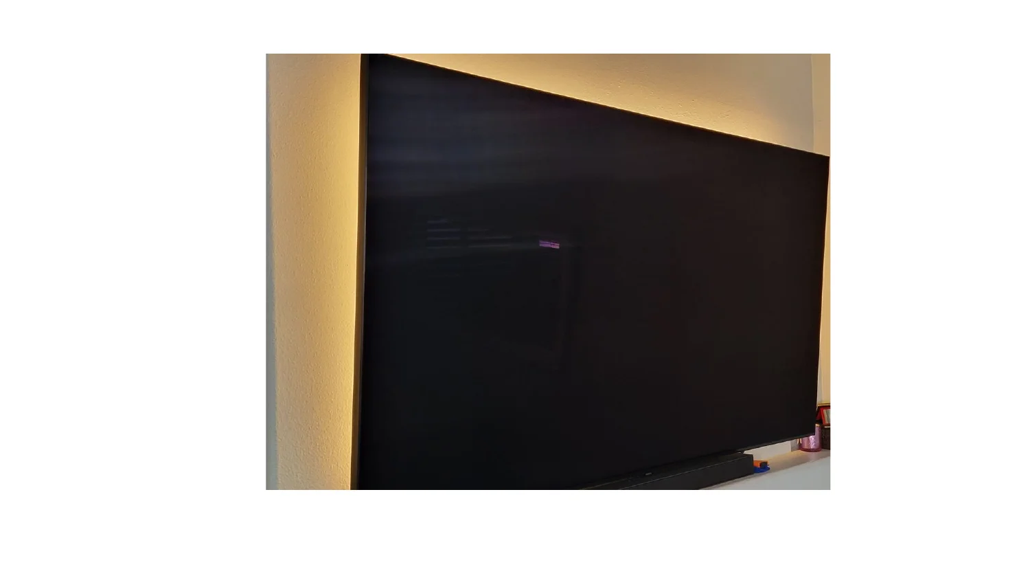 A large wall-mounted TV with warm backlighting glowing against the wall